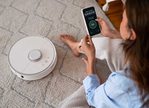 Woman controlling a robotic vacuum cleaner with smartphone app.