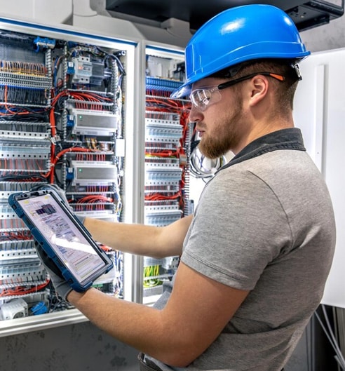 Technician in safety gear working on electrical control panel.