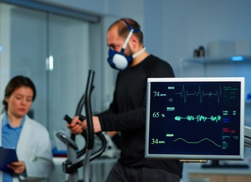 Healthcare professional using exercise equipment with patient monitoring screen.