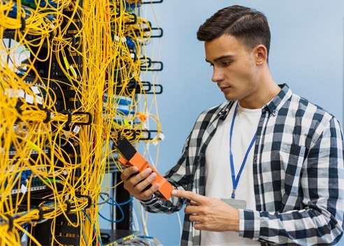 Young technician inspecting network cables and equipment in server rack.