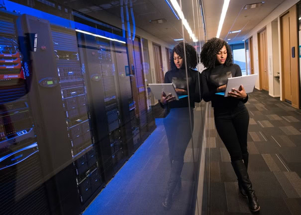 Woman working on a tablet in a data center corridor with server racks.