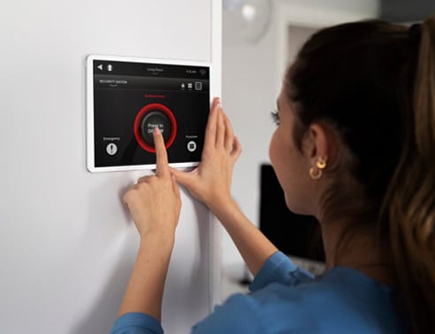 Woman adjusting smart home thermostat on wall.