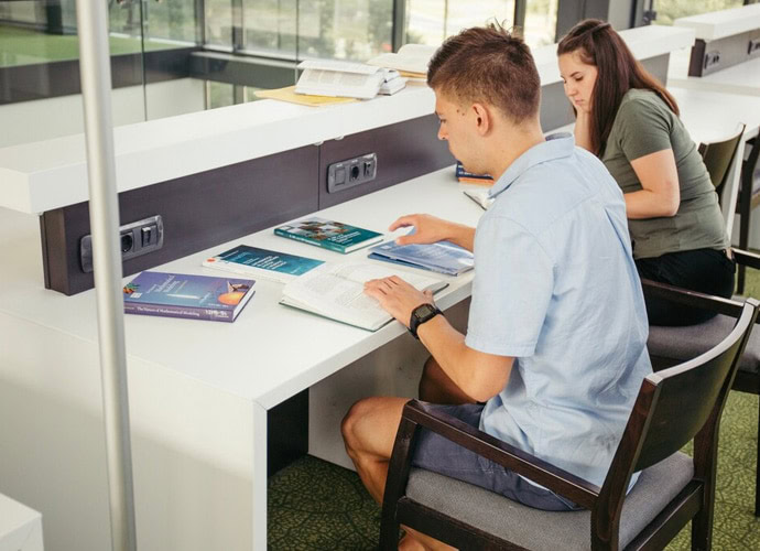Students studying with books and tablets in a bright classroom setting.