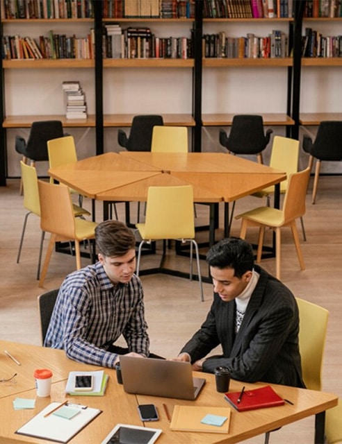 Students working together in a library study area with bookshelves.