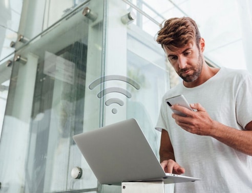 Young man using smartphone and laptop in modern office.