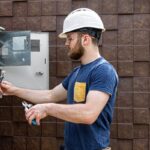 Electrician inspecting utility hub electrical panel with tools.